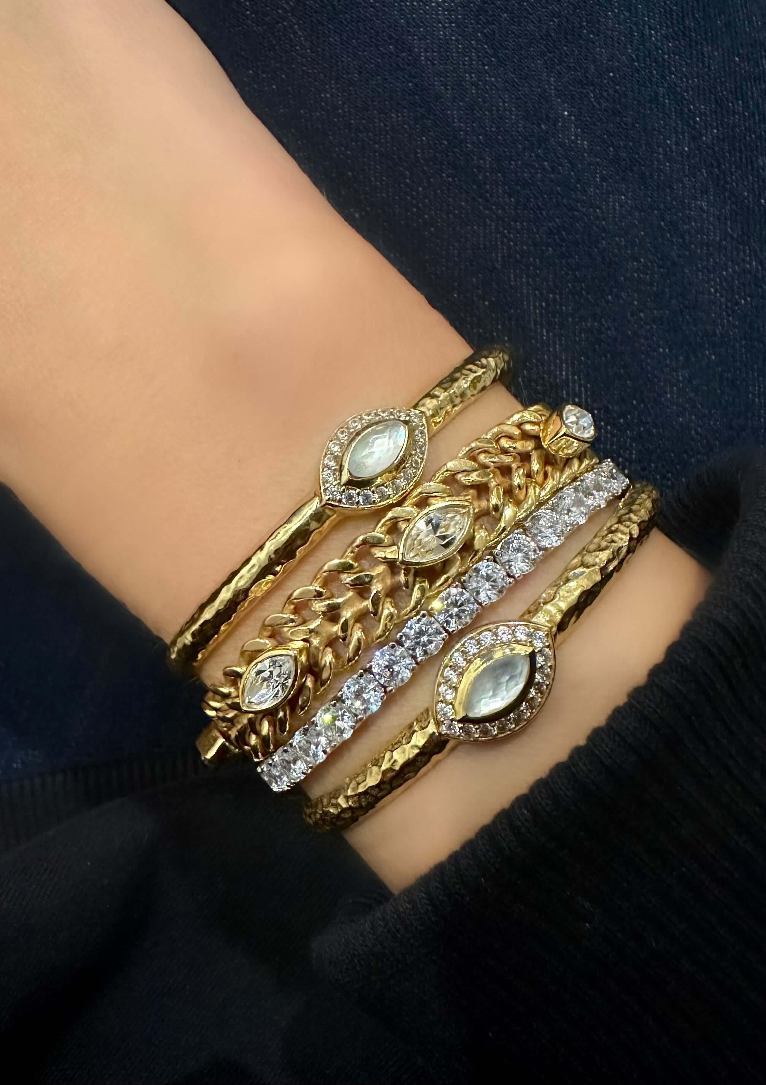 Collection of gold and silver bracelets adorned with sparkling gemstones displayed on wrist, showcasing luxurious jewelry design.
